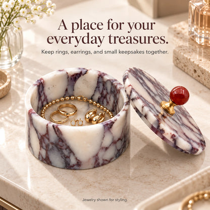 Purple marble jewelry box storing gold rings, earrings and a bracelet, with its removable red-knob lid resting beside it.
