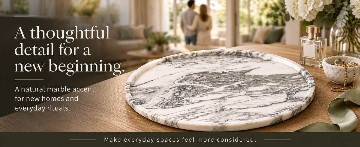 Grey marble round tray displayed on a wooden table beside perfume, jewelry, and flowers in a sunlit home.