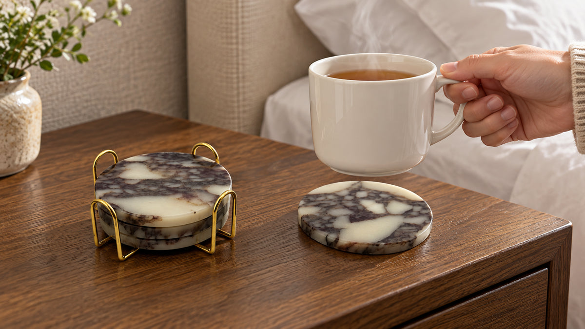 Load video: Marmor beige travertine coasters with textured stone surfaces and a gold-tone holder. The video shows close-up details, use with drinkware and cookware, rinsing under running water, and storage in the holder.