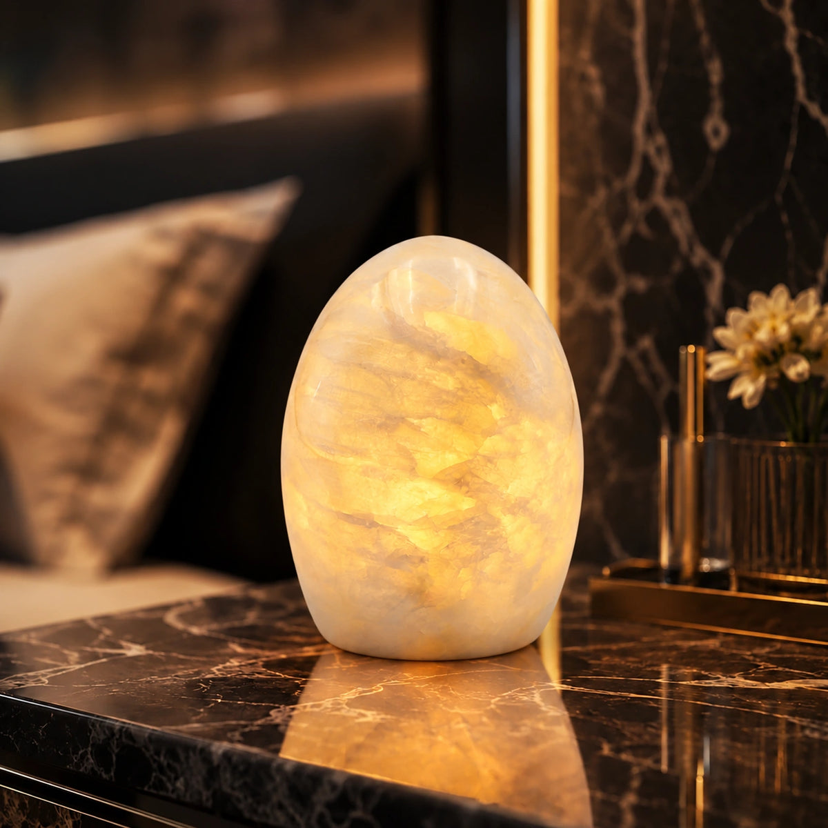 Glowing natural marble egg lamp with soft ivory veining displayed on a black marble bedside table in a luxurious bedroom.