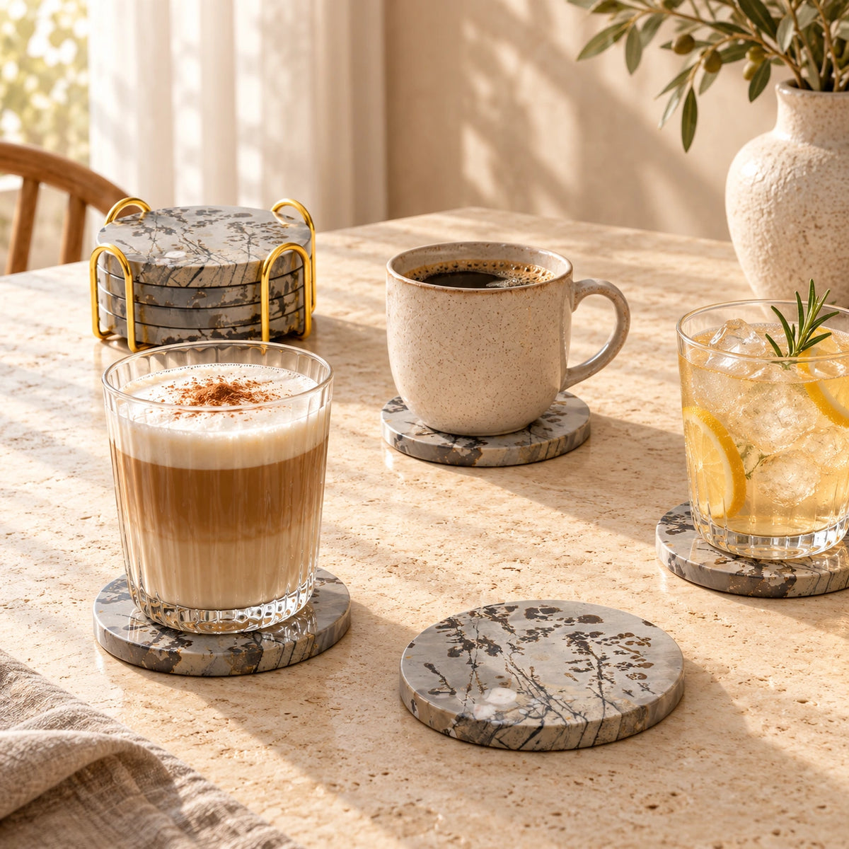 Guohua stone coasters beneath coffee and iced drinks, with a matching set in a gold-tone holder on a sunlit table.