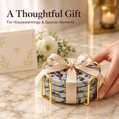 Four Guohua stone coasters in a gold-tone holder tied with a cream ribbon beside a greeting card and flowers.